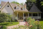 Beige and brown cottage style home with red Monarda flowers in garden at summer, Quebec, Canada