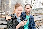 Couple checking messages on park bench, New York, New York, USA