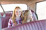 Two young girls sitting in back seat of car, smiling