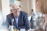 Senior businessman talking to businesswoman at breakfast table in hotel restaurant