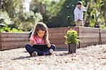 Girl sitting cross legged using digital tablet in community garden