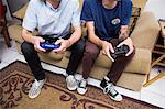Two young men sitting on sofa, playing video game, low section