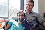 Male couple relaxing on sofa together with cat