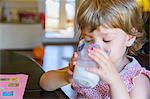 Cute young girl drinking glass of milk at kitchen table