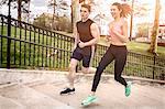 Young male and female runners running  up park stairway