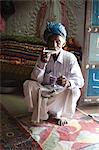 Turbanned man sipping tea from saucer in tribal home in front of piles of hand embroidered quilts, Soyla, Kachchh, Gujarat, India, Asia