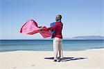 Man at the beach, holding blanket in the breeze