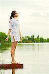 Woman standing at edge of lake dock with eyes closed