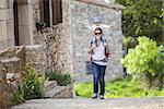 Young Caucasian woman tourist carrying her little son on shoulders while exploring old Spanish town