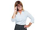 Charming middle aged female executive with one hand on waist while adjusting her eyeglasses.