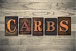 The word "CARBS" theme written in vintage, ink stained, wooden letterpress type on a wood grained background.