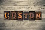 The word "CUSTOM" theme written in vintage, ink stained, wooden letterpress type on a wood grained background.