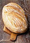 Big Loaf of Homemade Wheat Bread Full Body on Wooden Cutting Board closeup on Dark Wooden background