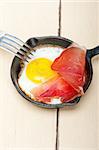 fried egg sunny side up with Italian tyrolean speck smoked ham on a skillet