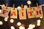 The word FAITH printed on clothespin clipped cards in front of defocused glowing lights.