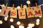 The word ISLAM printed on clothespin clipped cards in front of defocused glowing lights.