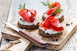 Snack rye bread, soft cheese with herbs and salted red salmon on a cutting board.