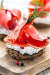 Sandwich of black bread, cheese with herbs and red salmon close up.