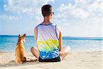 dog and owner sitting close together at the beach on summer vacation holidays, watching sunset or sunrise