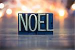 The word NOEL written in vintage metal letterpress type on a soft backlit background.