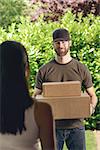 Woman answering the door to an attractive bearded deliveryman carrying two cardboard cartons for delivery, view over her shoulder from behind