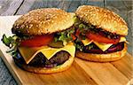 Homemade Hamburgers with Beef, Tomato, Lettuce, Pickle, Red Onion and Cheese into Sesame Buns closeup on Wooden Cutting Board