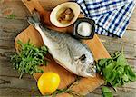 Cooking Raw Dorado Fish with Arugula, Herbs, Spices, Anchovies and Lemon on Wooden Cutting Board closeup. Top View