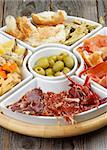 Arrangement of Spanish Snacks with Various Cheeses, Jamon, Cured Ham, Green Olives and Bread Sticks on Serving Plate closeup on Wooden background