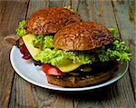 Homemade Hamburgers with Bacon Lettuce,Tomato, Onions, Cheese, and Pickled Cucumber with Whole Wheat Bun on White Plate closeup on Rustic Wooden background