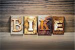 The word "BIKE" written in rusty metal letterpress type sitting on a wooden ledge background.