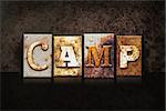 The word "CAMP" written in rusty metal letterpress type on a dark textured grunge background.