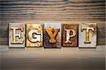 The word "EGYPT" written in rusty metal letterpress type sitting on a wooden ledge background.