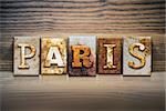 The word "PARIS" written in rusty metal letterpress type sitting on a wooden ledge background.