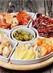 Arrangement of Spanish Snacks with Various Cheeses, Bread Sticks, Jamon, Cured Ham and Green Olives on Serving Plate closeup on Wooden background
