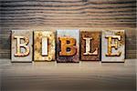 The word "BIBLE" written in rusty metal letterpress type sitting on a wooden ledge background.