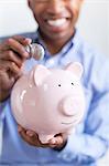 Young man putting coin in piggybank