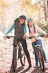 Portrait smiling mother and daughter on mountain bikes in woods