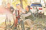 Father fastening helmet of son on bicycle in autumn woods