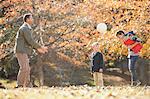 Father and sons playing soccer in autumn park