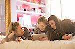 Teenage girls using cell phones and digital tablet on bed