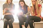 Teenage girls texting with cell phones in kitchen