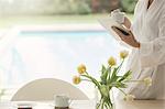 Woman in bathrobe drinking coffee and using digital tablet at poolside