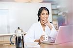 Portrait smiling woman in bathrobe drinking coffee at laptop