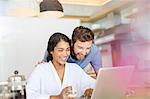 Laughing couple drinking coffee and using laptop