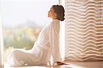 Serene woman in bathrobe sitting cross-legged at sunny doorway