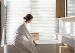 Woman in bathrobe drawing a bath in soaking tub in luxury bathroom