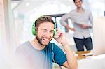 Smiling creative businessman listening to headphones in office
