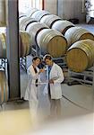 Vintners in lab coats examining wine in winery cellar