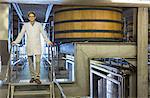 Portrait confident vintner in lab coat on platform in winery cellar