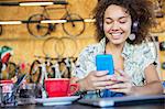 Smiling woman with headphones texting on cell phone in bike shop